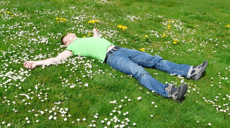 man laying on daisy covered grass relaxing