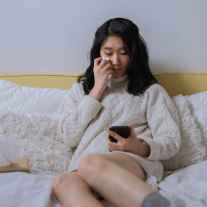 woman sitting on bed looking at her cell phone while crying