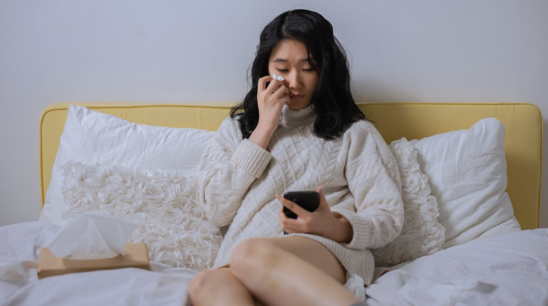 woman sitting on bed looking at her cell phone while crying