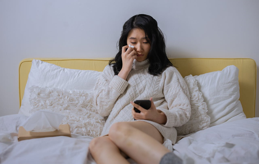 woman sitting on bed looking at her cell phone while crying