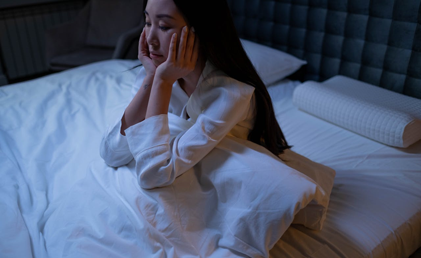 woman struggling with insomnia sitting up in bed at night