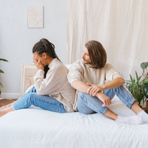 Upset woman sitting on bed with her partner