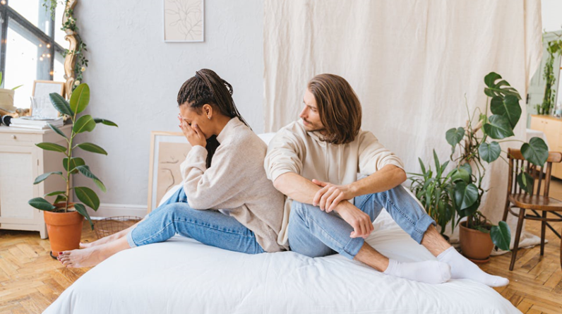 Upset woman sitting on bed with her partner