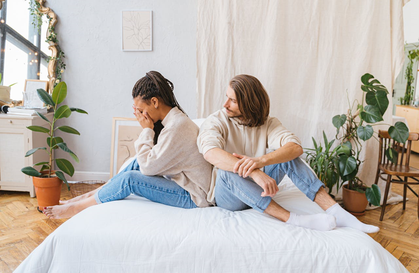 Upset woman sitting on bed with her partner