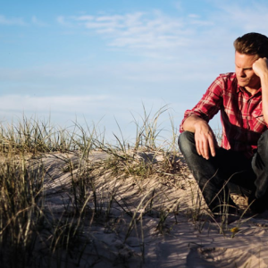 man sitting outside at the beach looking sad