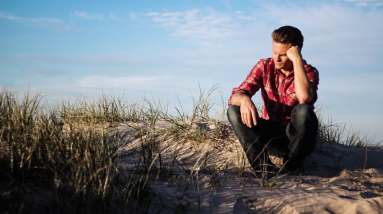 man sitting outside at the beach looking sad