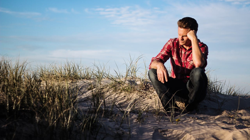 man sitting outside at the beach looking sad