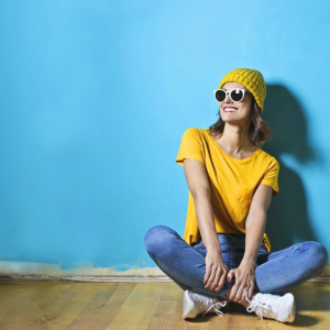 happy woman in bright yellow top sitting in front of blue wall