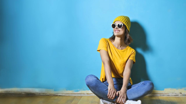 happy woman in bright yellow top sitting in front of blue wall