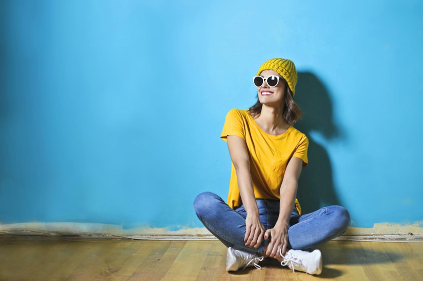 happy woman in bright yellow top sitting in front of blue wall