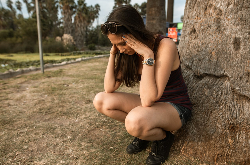 woman crouching down next to tree looking worried and anxious