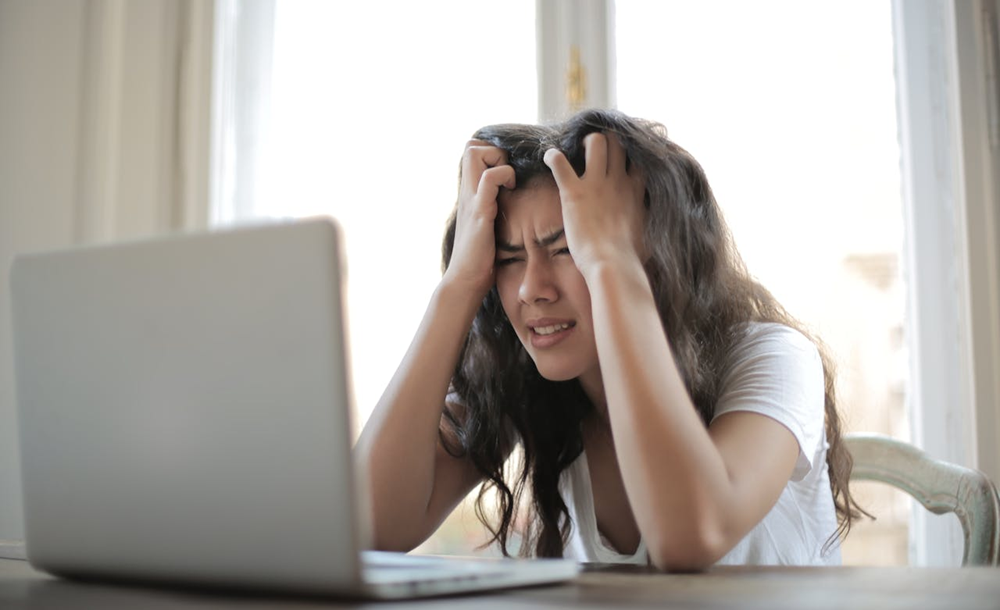 woman looking very stressed while looking at her laptop